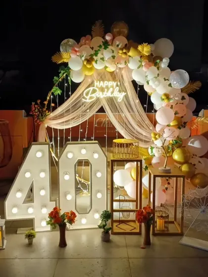 A beautiful boho-chic setup for a 40th birthday. The decor includes a draped arch, pampas grass, and large light-up numbers.