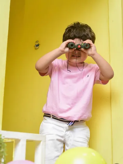 I spy with my little eye! A boy uses binoculars to explore the play area from a new perspective.