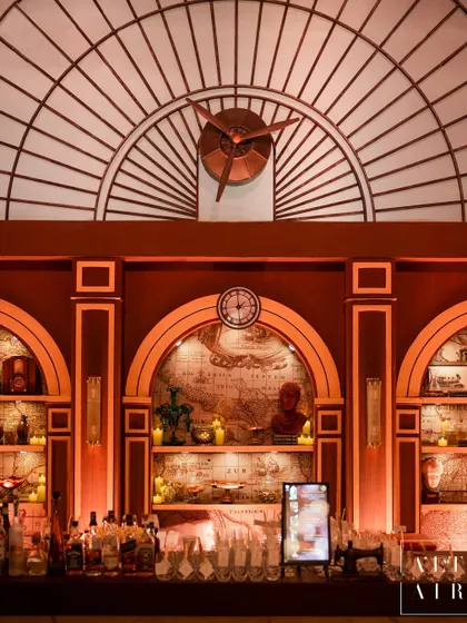 The bar area was designed with intricate details reminiscent of a vintage train station, including a large clock, an arched window, and shelves filled with travel-themed artifacts and warm candlelight.