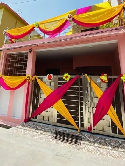 The entrance gate and balcony of a house decorated with bright yellow and pink drapes and floral accents.