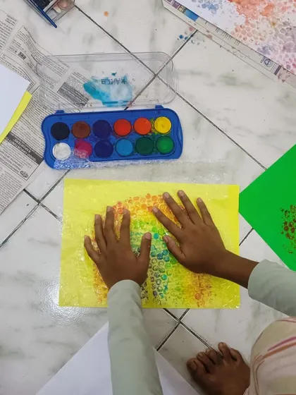 A close-up of a child's hands pressing bubble wrap onto a painted surface. This sensory activity is a perfect example of process art, where the experience is as important as the final product.