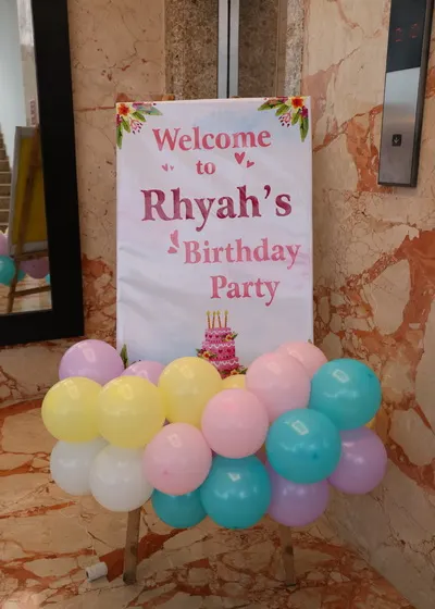 A simple and clear welcome sign for a child's birthday party. The easel is decorated with a small balloon cluster at the base to match the party's color scheme.