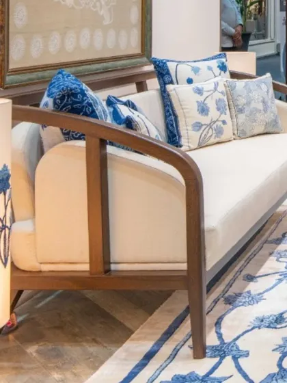A custom-designed sofa with a gracefully curved wooden frame, upholstered in natural Khadi and adorned with indigo-print cushions. The piece feels both elegant and inviting.