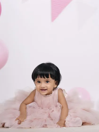 All smiles during this first birthday studio session. The simple setup with pink balloons and a festive banner keeps the focus on the baby's joyful personality.