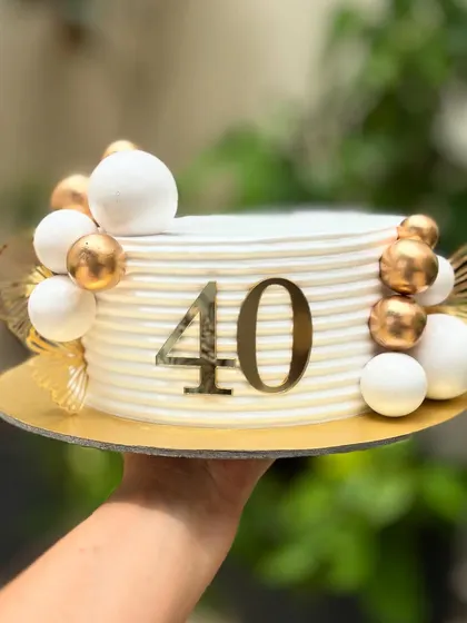 Forty and fabulous. This chic cake for a 40th birthday has a clean, ribbed buttercream finish, decorated with white and gold spheres and a bold number topper.