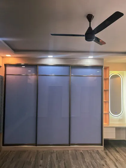 Floor-to-ceiling wardrobes help maximize storage and make a room look larger. This design features back-painted glass sliding shutters and an integrated dresser with a backlit mirror.
