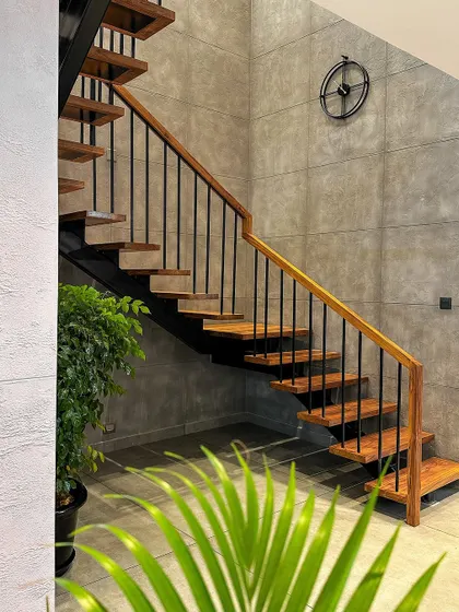 A simple yet elegant staircase in a Payyannur project, featuring wooden steps and a classic black metal spindle railing against a concrete-finish wall.