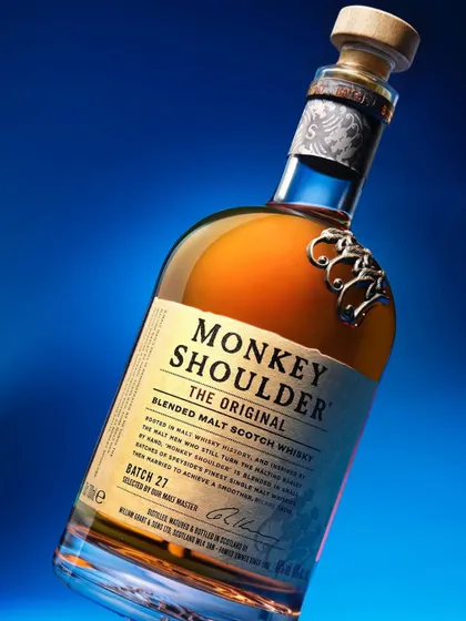 An experimental shot of a Monkey Shoulder whiskey bottle. The dynamic angle and bold blue background lighting make the bottle feel modern and exciting, perfect for social media or ad campaigns.