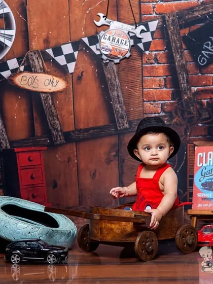 A baby boy in a red outfit sits in a wooden wagon in our classic garage set. The backdrop, filled with tires, tools, and vintage signs, creates a fun and masculine theme for a toddler shoot.