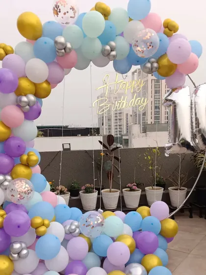 A pastel-themed 10th birthday party on a rooftop. This setup features a large balloon ring with a city view, a clear "Happy Birthday" sign, and a silver number '10' foil balloon.