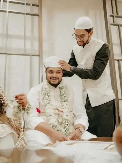 A candid moment during a Nikah ceremony, where a family member adjusts the groom's cap, showing the love and support of family.