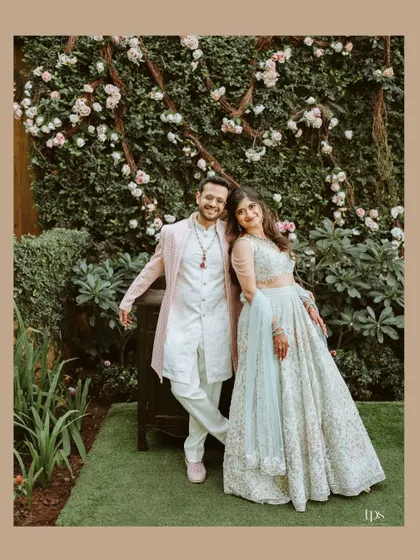 A relaxed portrait of Avi and Devika against a wall of flowers. Their casual poses and happy expressions create a warm and inviting image.