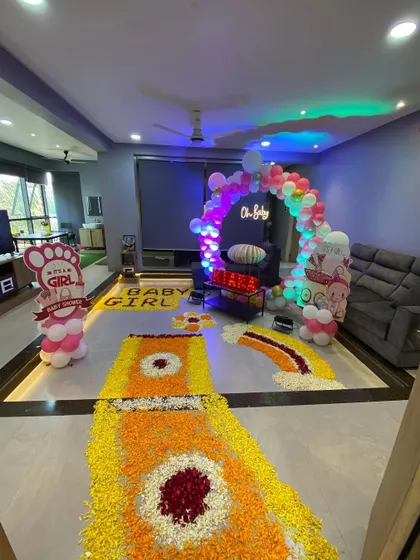 A full view of a living room decorated for a baby's homecoming, with a flower rangoli path and a balloon arch.