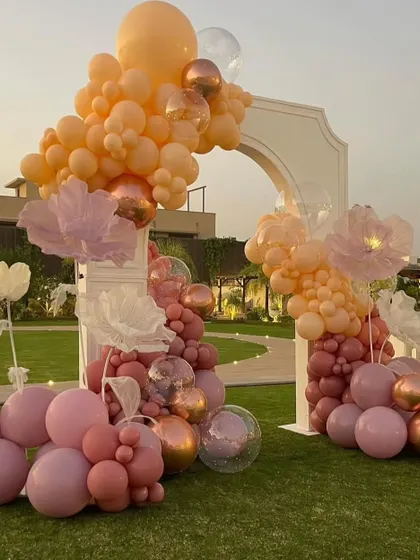 A wider view of the beautiful balloon arch set against the lush green lawn and sunset sky, creating a perfect photo backdrop.