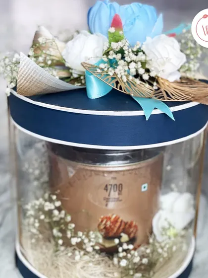 This cylindrical acrylic box showcases a tin of gourmet popcorn, surrounded by delicate baby's breath. It's a modern and chic way to present a simple yet delicious treat.