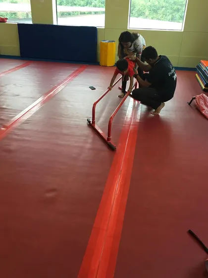 A father and coach work together to help a child practice on a mini bar, showing how we partner with parents to support their child's journey.