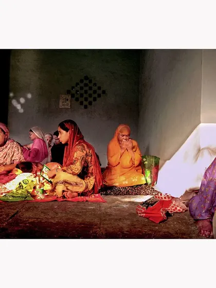 A group of women gathered in prayer. The soft light illuminates the room, creating a quiet, intimate atmosphere. This documentary photograph captures a moment of shared faith and community.