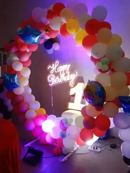 A colorful and joyful first birthday setup featuring a multi-colored balloon ring and a light-up number '1'.
