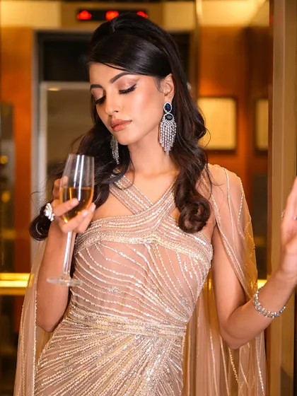 A moment of elegance with a glass of champagne. The makeup is sophisticated and chic, designed to look flawless in the warm, ambient light of an evening event.