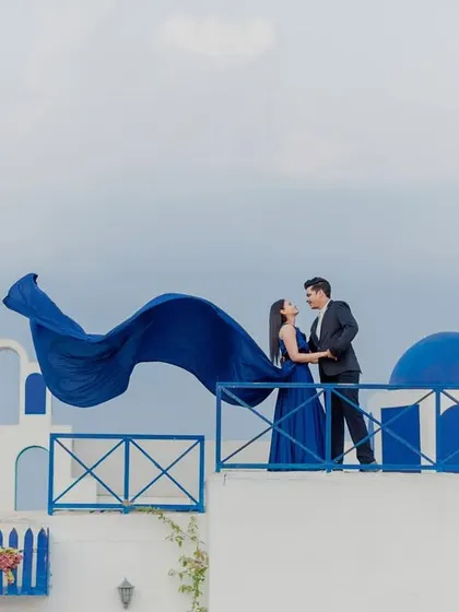 A wide, cinematic view of the Santorini-style set, with the flowing blue dress creating a sense of movement and freedom.