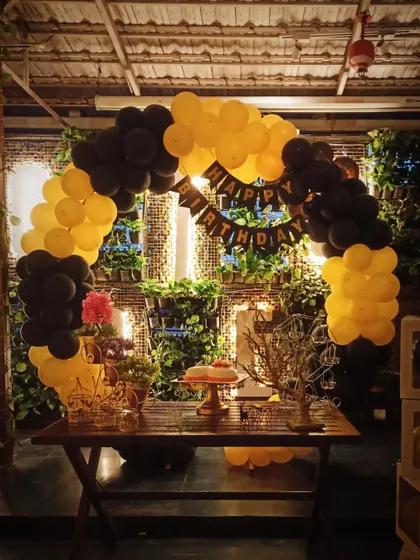A modern and stylish balloon arch in a striking yellow and black color scheme. Set against a natural green wall, this setup includes a 'Happy Birthday' banner and transparent 'BABY' blocks for a chic, contemporary feel.