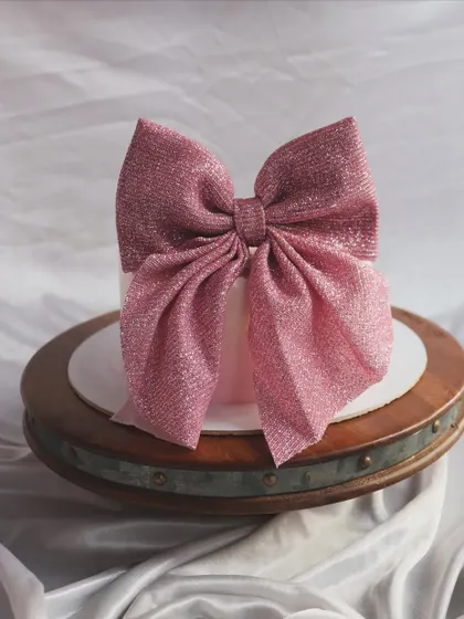 A simple and elegant cake topped with a large, sparkly pink bow.