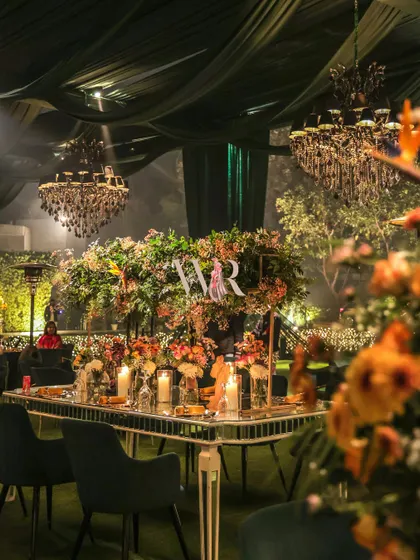 A romantic tablescape from a 'Garden of Dreams' engagement. The mirrored table reflects the glow of candles and the lush, colorful floral arrangements, all set under a canopy of green drapes and sparkling chandeliers.
