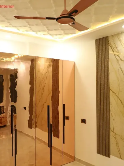 This bedroom features a unique wardrobe with rose-gold tinted mirror doors, which adds a touch of glamour and reflects light beautifully. The room also has a textured ceiling and a stone-paneled wall.