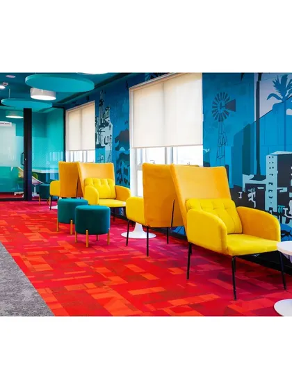 This lounge corridor at Mindsprint is brought to life with a striking blue mural and high-backed yellow armchairs. The vibrant red carpet and modern furniture create a stylish and comfortable passage between different office zones.