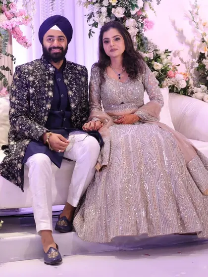 A picture of pure elegance from a client's sangeet night. Seated amidst a beautiful floral backdrop, their coordinated outfits truly stand out. His richly embroidered navy sherwani and her shimmering silver lehenga were designed to be the perfect pair.