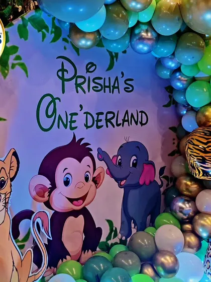 A close-up of our jungle-themed 'Onederland' backdrop. This shot highlights the custom-printed background featuring characters like Simba, Dumbo, and a monkey, surrounded by a green and metallic balloon arch.