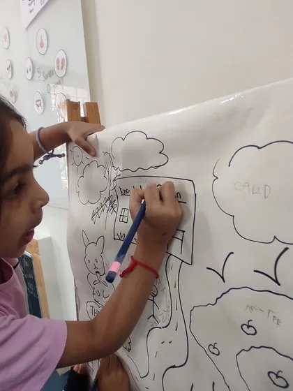 A close-up of a child carefully writing the name of our school on her drawing. This shows the development of fine motor skills and pre-writing abilities through art.
