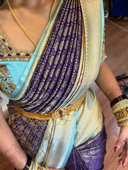 A close-up of a modern draping style on a beautiful light blue and purple silk saree. The pleats are neatly gathered at the shoulder for a contemporary feel.