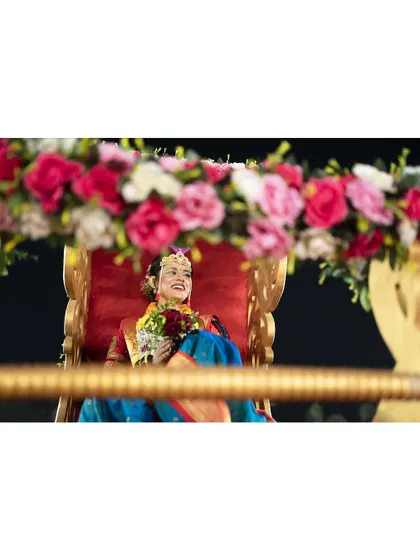 The bride's joyful entrance on a beautifully decorated doli. This candid shot captures her happiness and the grandeur of the wedding celebration.
