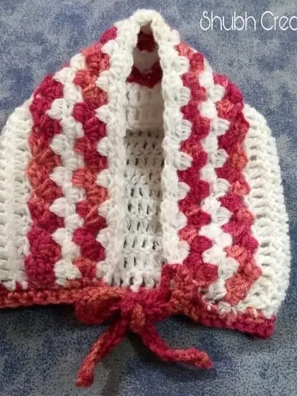 A close-up of the granny-square style baby bonnet in shades of pink and white, part of a matching dress set.