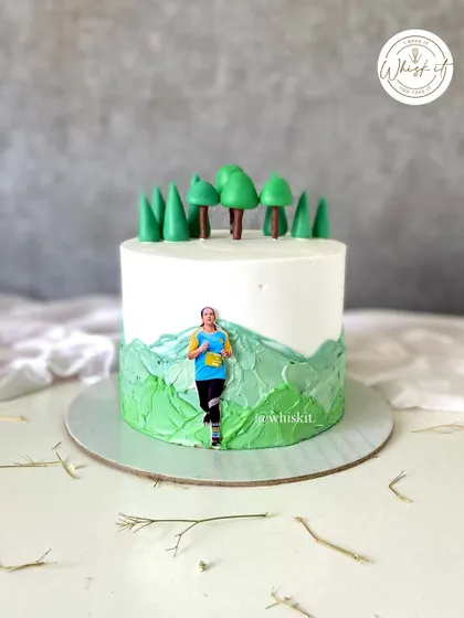 A custom cake for a runner, personalized with an edible print of her photo. The design features a landscape of green hills and trees, celebrating her passion for running.