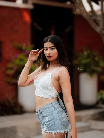 A confident and relaxed street fashion shot. The red building in the background adds a warm, vibrant contrast to the model's casual white and denim outfit.