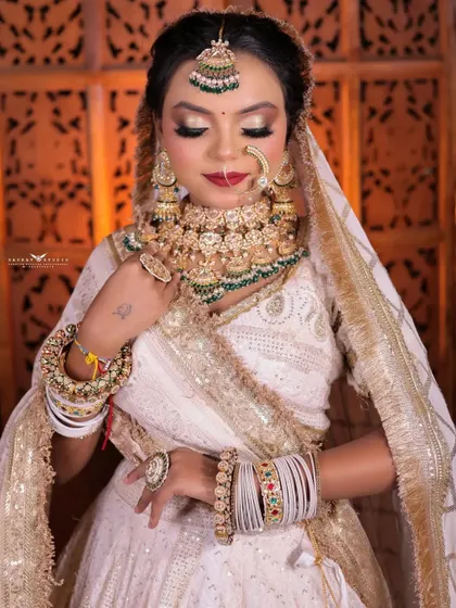 A close-up shot with the bride's eyes closed, highlighting her shimmering eyeshadow and flawless makeup. The white and gold outfit provides a perfect, luminous frame.