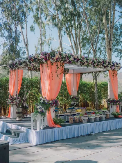 A beautiful food stall setup at an outdoor wedding, draped in peach fabric and adorned with flowers. I believe every part of the wedding, including the catering, should be beautiful.