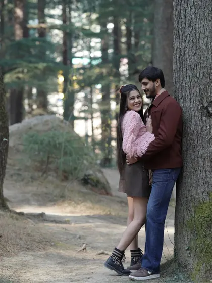 A happy, natural portrait of a couple leaning against a tree in a sunlit forest, showcasing their easy and comfortable love.