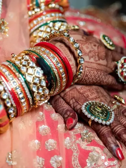 A stunning close-up of the bride's hands, adorned with elaborate henna, rings, and a colorful stack of wedding bangles (chooda).