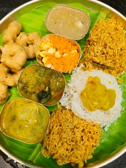A traditional meal served on a banana leaf, featuring various dishes prepared for a festival. This includes vade, payasa, and different kinds of rice.