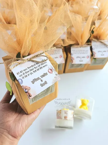 Holding one of the finished teddy bear candle gift boxes, showcasing the rustic jute tie, net wrapping, and personalized card.