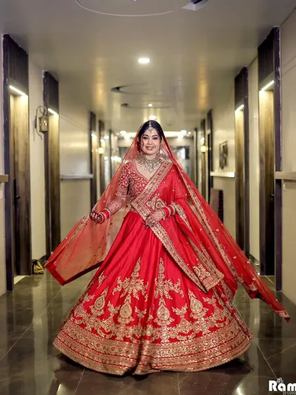 A full-length shot of the bride showing off her magnificent red lehenga with a wide, happy twirl in a hotel corridor.