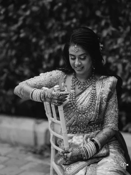 A timeless black and white portrait of the bride seated, her intricate jewelry and beautiful saree on full display.