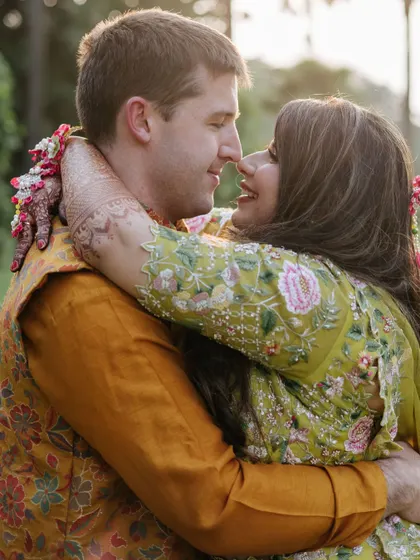 A romantic, happy moment between the couple at their Mehndi. The bride's vibrant floral lehenga is paired with a fresh and dewy makeup look.