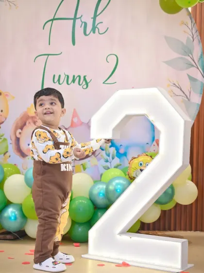 The birthday boy stands proudly next to a large, light-up number '2' at his jungle-themed party.
