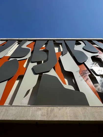 A low angle view of the "Framed Austerity" facade against a clear blue sky. The artwork's layers of grey, white, and orange create a powerful graphic statement, showcasing how I use art to give a building a unique identity.