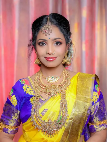 A beautiful South Indian bridal portrait. The bride's bright yellow and blue saree, combined with her elaborate gold temple jewelry, creates a vibrant and traditional look.