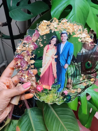 I also create personalized resin photo frames to preserve your cherished memories. This piece encases a couple's photo with dried rose petals, gold flakes, and a peacock feather for a touch of elegance.